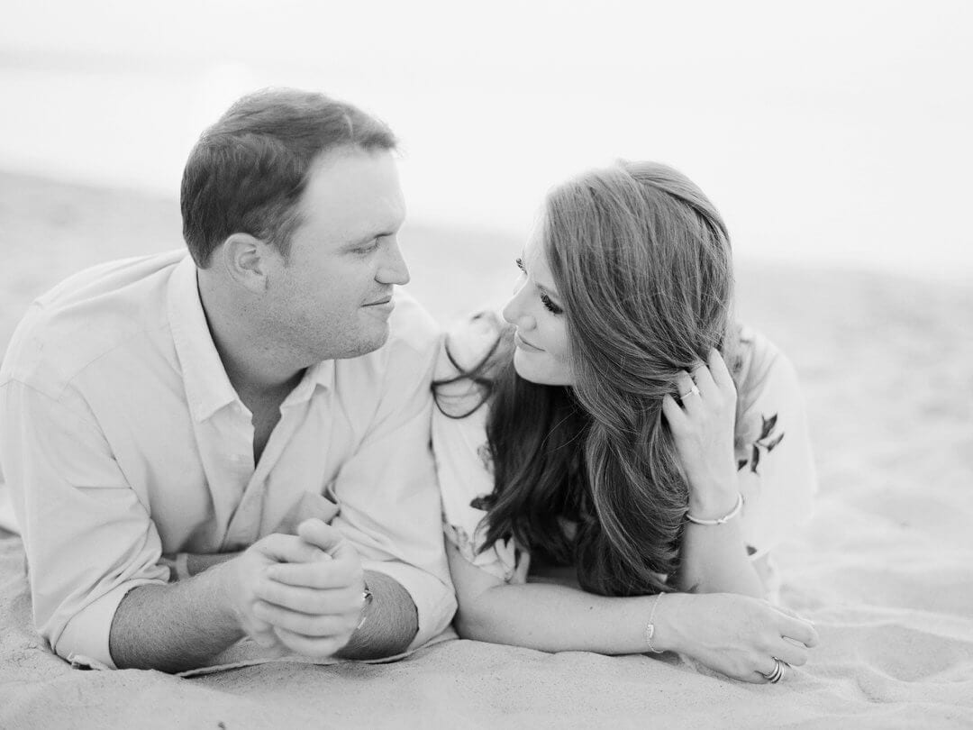 couple at engagement session on the beach lying in the sand together