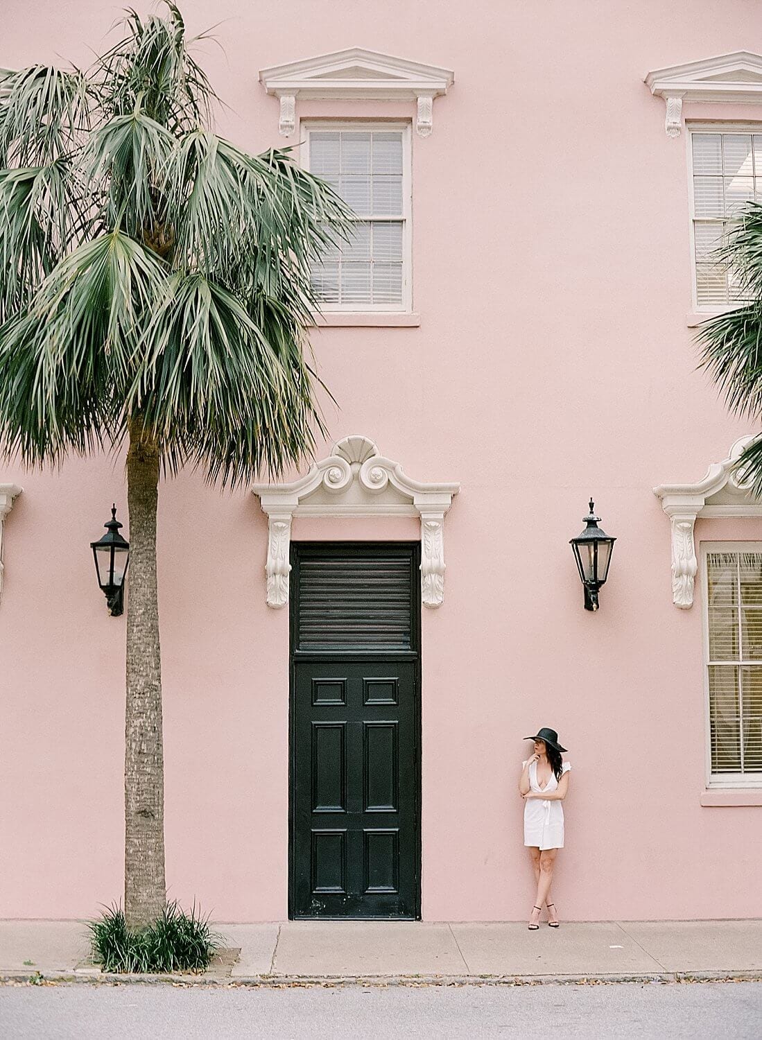 An editorial at The Mills House in Charleston utilizing a model in a white dress and black hat against a beautiful colorful pink wall.