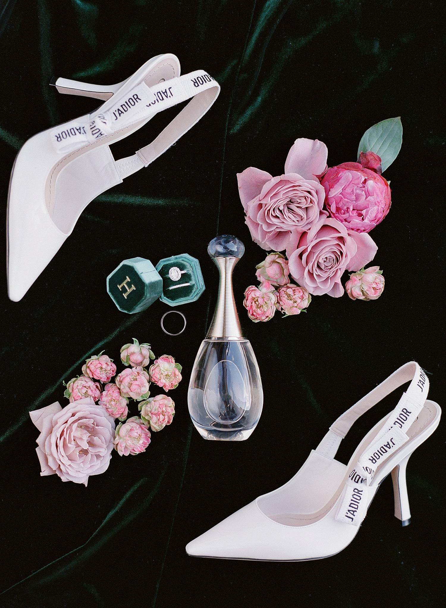 Dior perfume and heels with wedding bands and florals on green velvet.