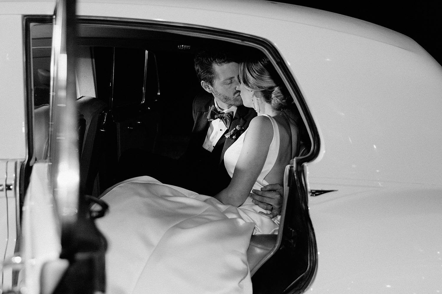 Bride and groom sharing a kiss in vintage car before leaving their wedding at Dover Hall Estate