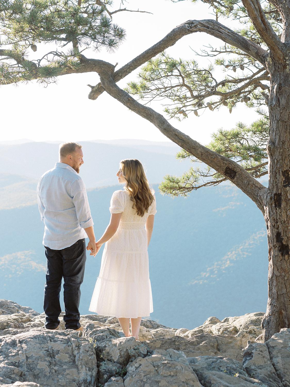 Bride and groom holding hands looking out on the Blue Ridge Mountains during their engagement session at Ravens Roost.