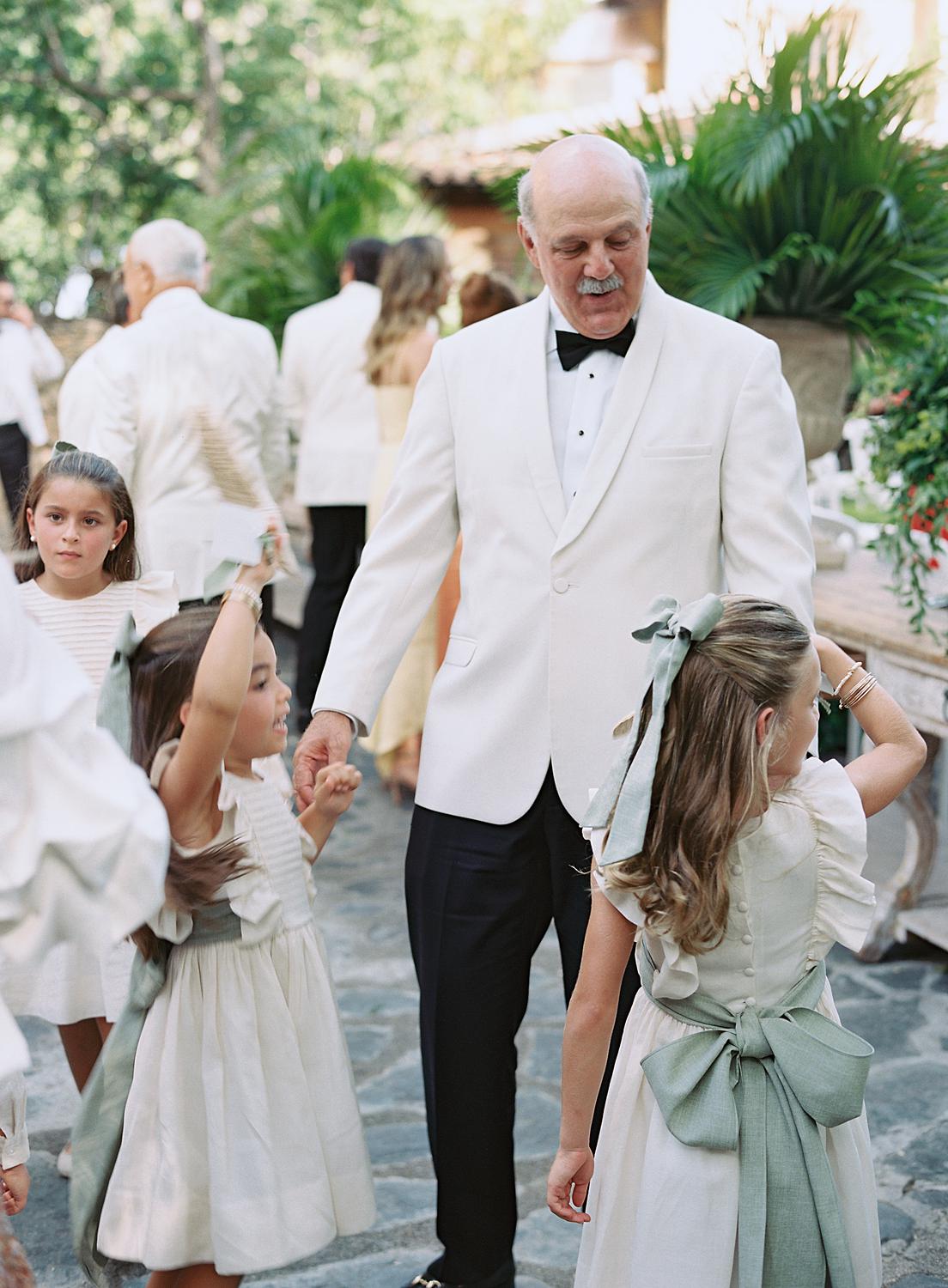 Grandfather white dinner jacket playing with flower girls before an Altos de Chavón wedding.
