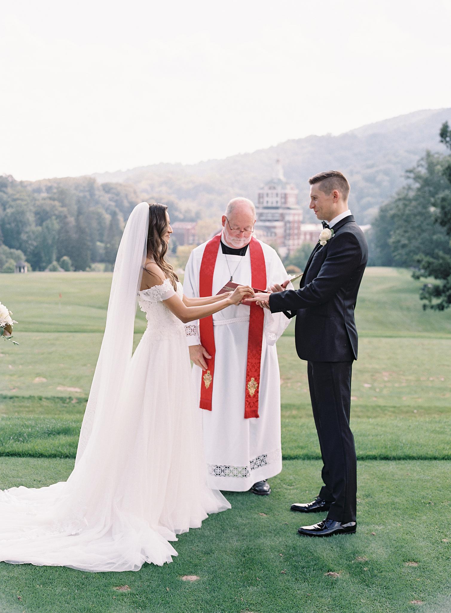 Bride and groom exchanging rings at their ceremony overlooking The Omni Homestead Resort.