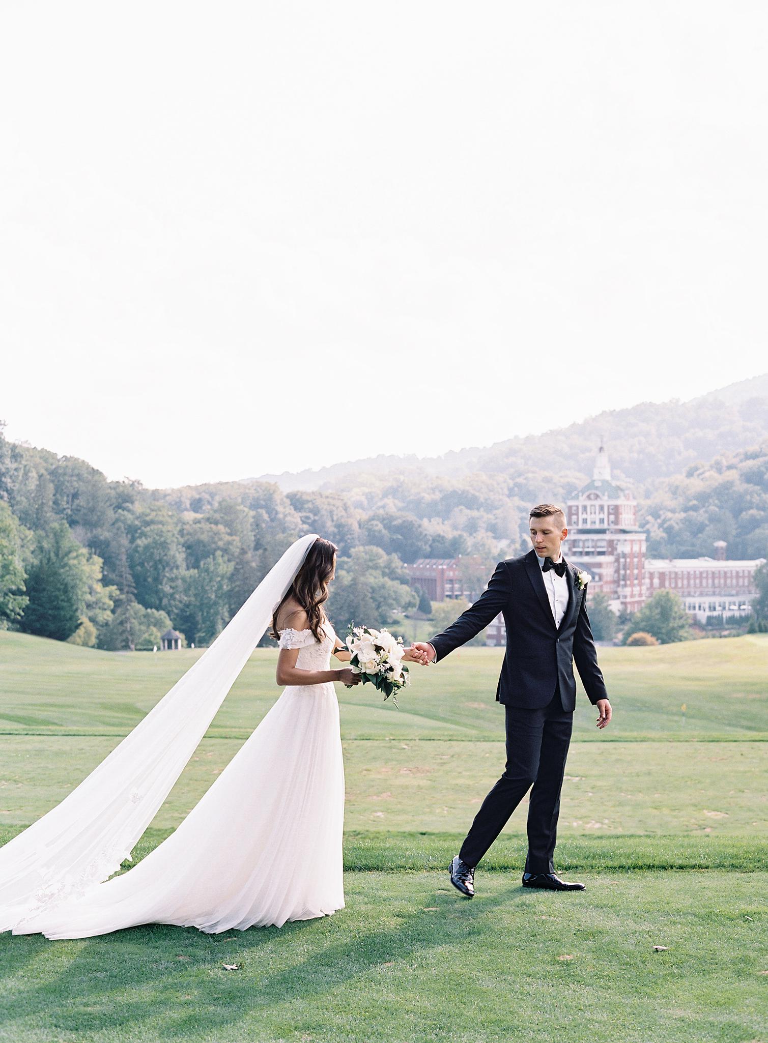 Groom leading bride across the lawn during their wedding portraits.