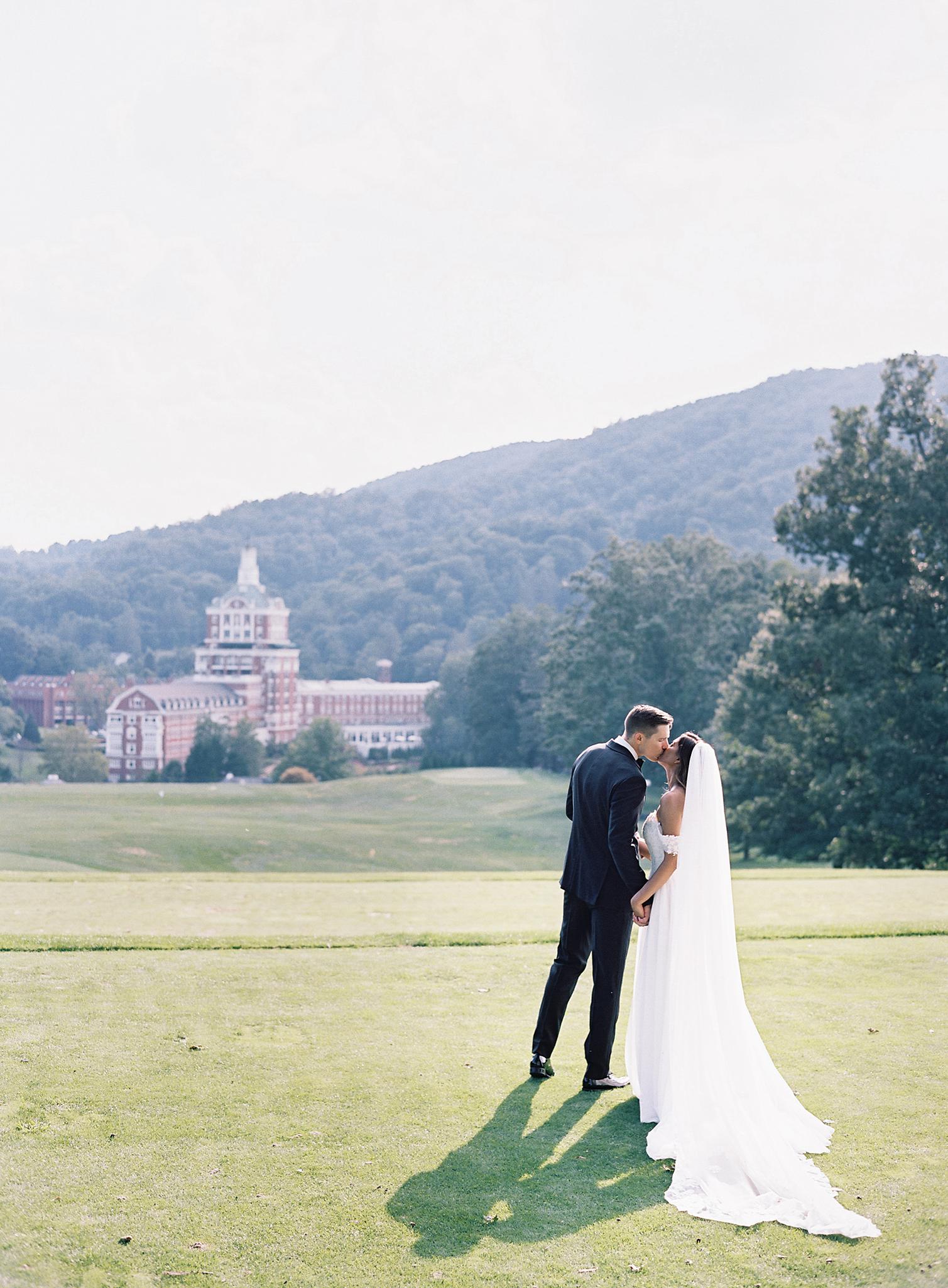 Bride and groom kissing on the lawn overlooking The Omni Homestead Resort.