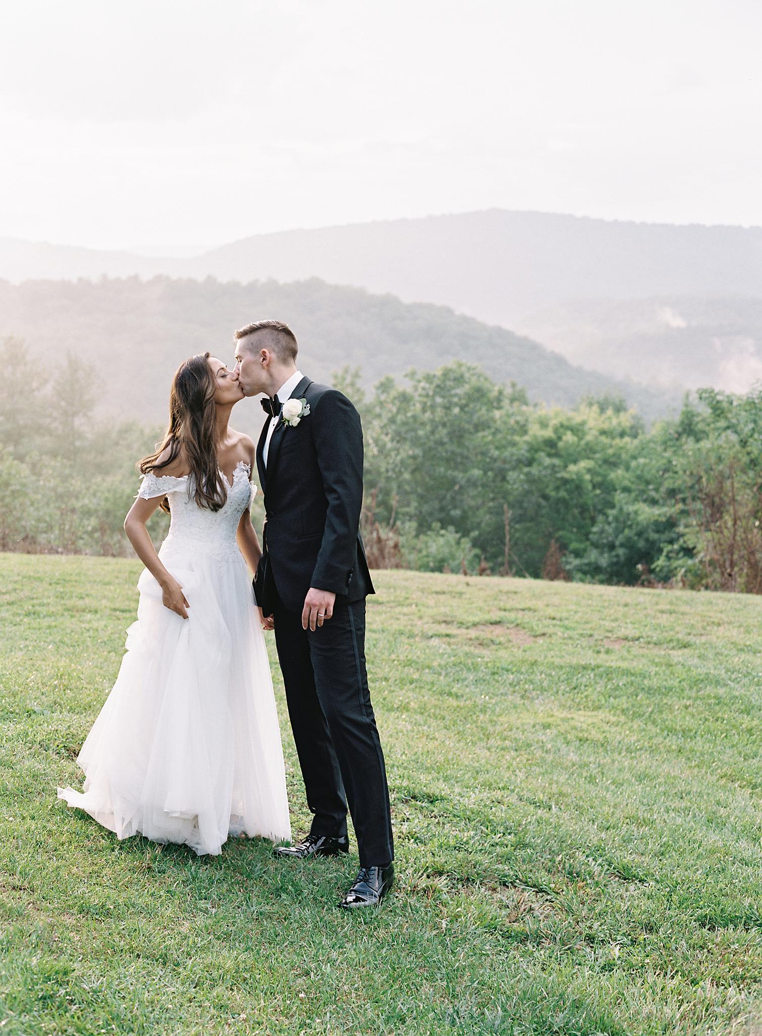 Bride and groom kissing in meadow overlooking the blue ridge mountains at their Omni Homestead Resort wedding.