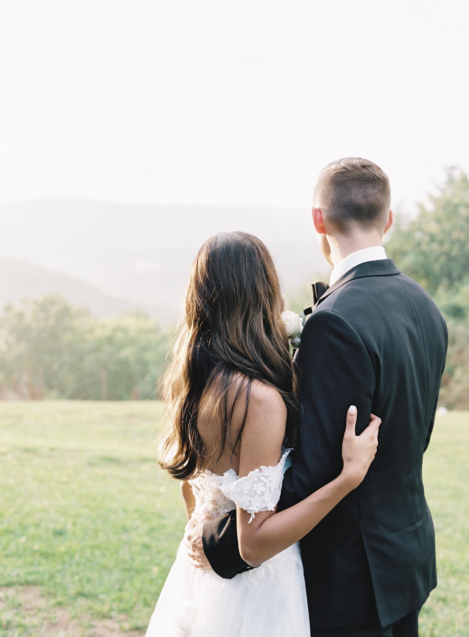 Bride and groom embracing in meadow overlooking the blue ridge mountains at their Omni Homestead Resort wedding.