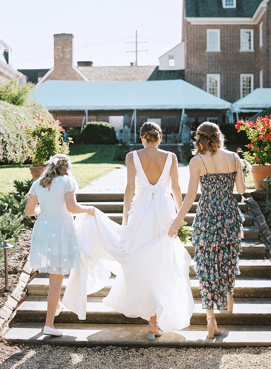 Bridesmaids helping bride with her dress as she walks up stairs at The William Paca House and Gardens.