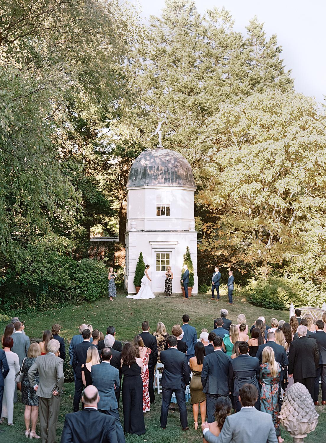 Photo of guests looking on as bride and groom marry each other during their William Paca House wedding.