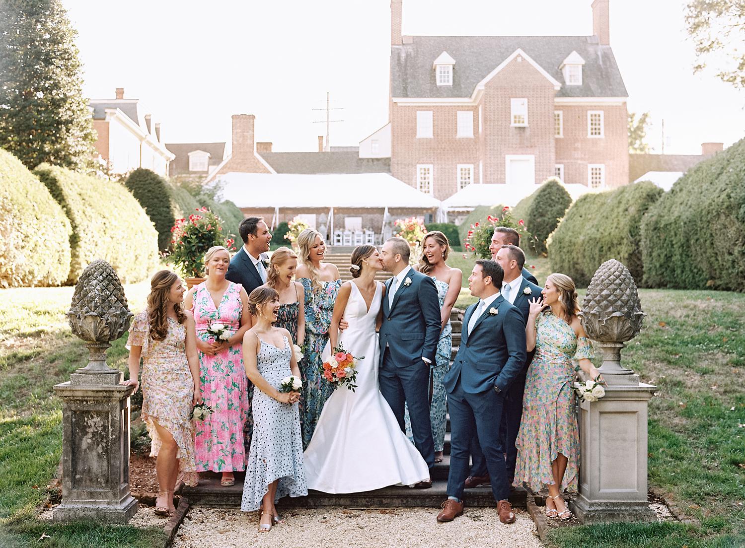 Bride and groom kissing during their bridal party portrait as bridal party cheers on.