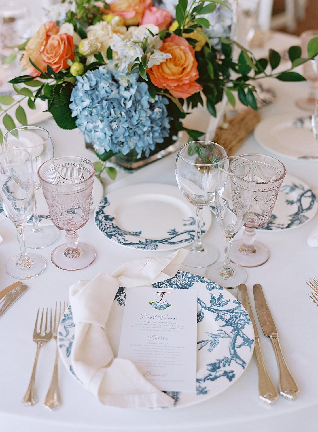 Detail shot of wedding reception table details of chinoiserie plate, colored water glasses and colorful centerpiece florals at William Paca House.