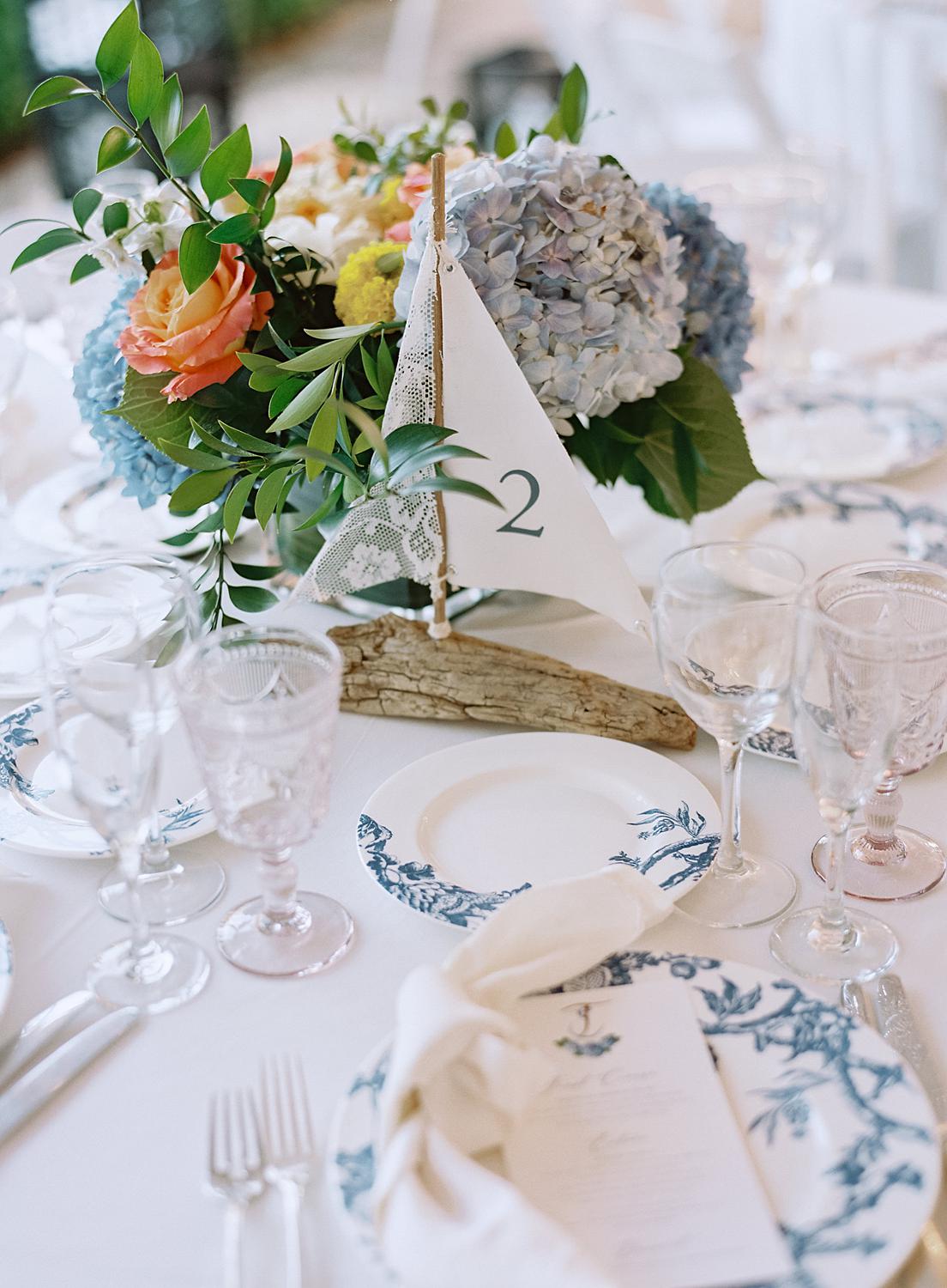 Detail shot of reception table settings with a handmade sailboat as the table number.